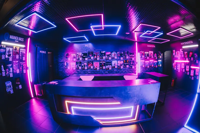 Espaço da Nuuvem na BGS visto de dentro, com balcão curvo, luminárias de neon em rosa e azul e pôsteres de jogos nas paredes.