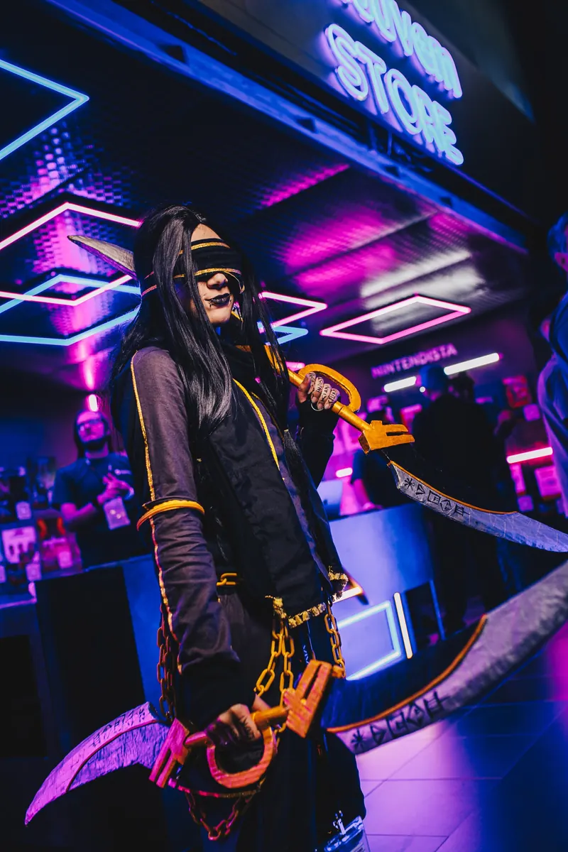 Cosplayer de venda nos olhos e longos cabelos pretos empunha duas lâminas curvas diante do letreiro de neon da loja.