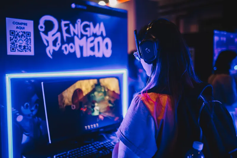 Visitante de fone de ouvido joga em um computador, ao lado de um painel azul do jogo Enigma do Medo.