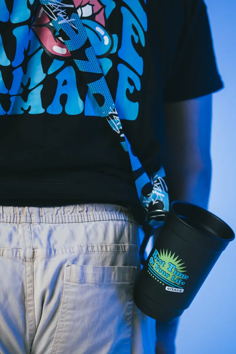 Detalhe de uma camiseta preta com estampa azul e de uma caneca preta pendurada na cintura por uma alça azul, em luz azul de estúdio.